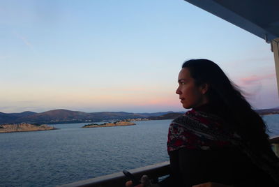 Woman looking away while standing by railing against sky during sunset