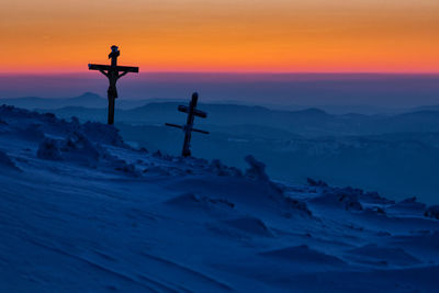 Silhouette crosses on snow covered mountain against sky during sunset