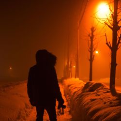 Rear view of silhouette man standing on snow covered landscape at night