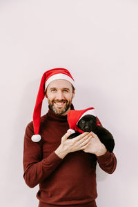 Male volunteer in a santa hat is holding a puppy with a santa hat.