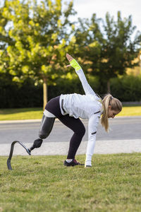 Side view of professional female runner with leg prosthesis preparing for explosive start during training in park