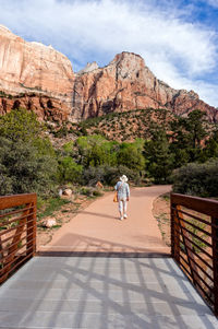 Rear view full length of person walking on footpath against rock formation