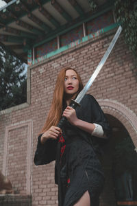 Portrait of young woman standing against brick wall