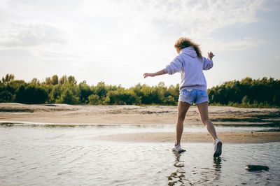 Rear view of woman balancing on rocks at beach against sky