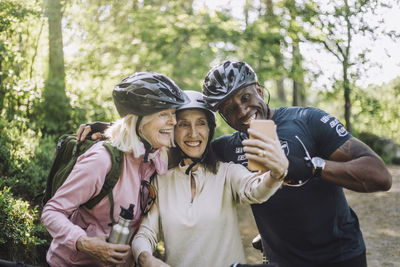 Smiling senior woman taking selfie through smart phone with male and female friend