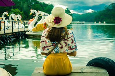 Rear view of woman in hat sitting at lakeshore