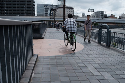 Man riding bicycle on bridge in city against sky