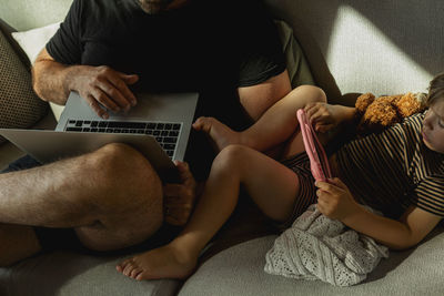 High angle view of male freelancer working on laptop with his son using digital tablet in living room