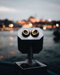 Close-up of coin-operated binoculars against sea at dusk
