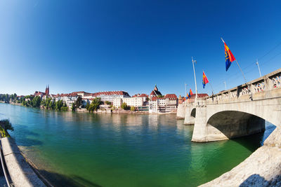 Bridge over river by city against clear blue sky