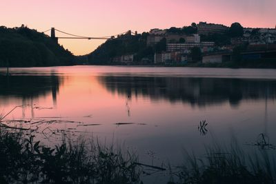 Scenic view of river by city against sky at sunset