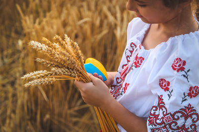 Midsection of girl holding heart shape with crops on field