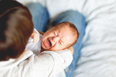 High angle view of mother carrying baby girl on bed at home