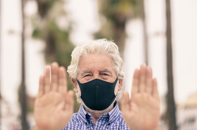 Portrait of senior man wearing mask gesturing outdoors