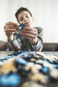 Cute boy playing with jigsaw pieces while sitting on table at home