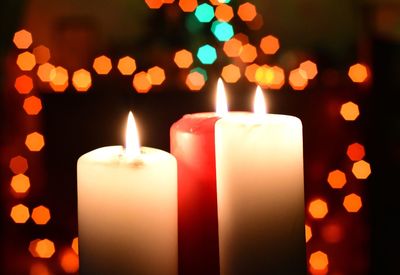 Close-up of burning candles against illuminated lights at night