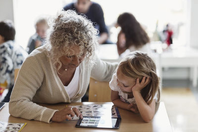 Senior teacher using digital tablet with student in preschool