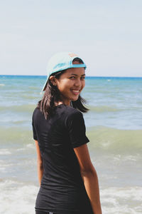 Portrait of smiling young woman standing at beach against sky