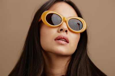 Close-up of young woman wearing sunglasses against wall