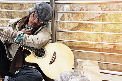 Homeless man sitting with guitar against railing