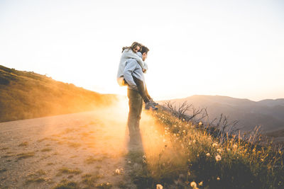 Side view of man carrying girlfriend on back at mountain road