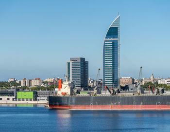 Modern buildings by river against clear blue sky