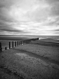 Wooden posts on beach by sea against sky