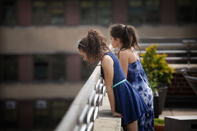 Side view of girls leaning on railing while standing at building terrace