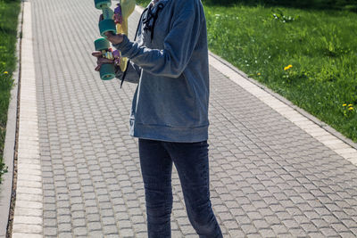 Midsection of man holding skateboard while standing on footpath