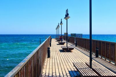 Pier over sea against clear blue sky