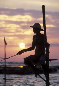 Fisherman against sea during sunset