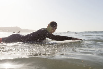 Side view portrait of happy male surfer lying on surfboard in sea during sunset