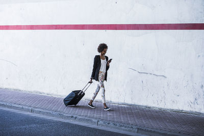 Walking businesswoman with baggage looking at her smartphone
