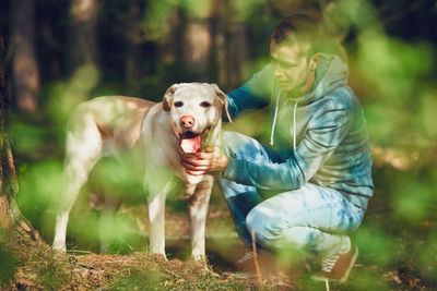 Young man crouching by dog on field at forest