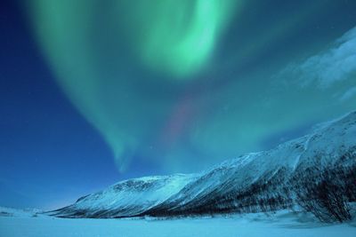 Idyllic view of northern lights over snowcapped landscape at dusk