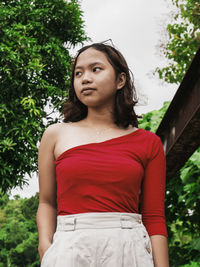 Young woman looking away while standing against trees