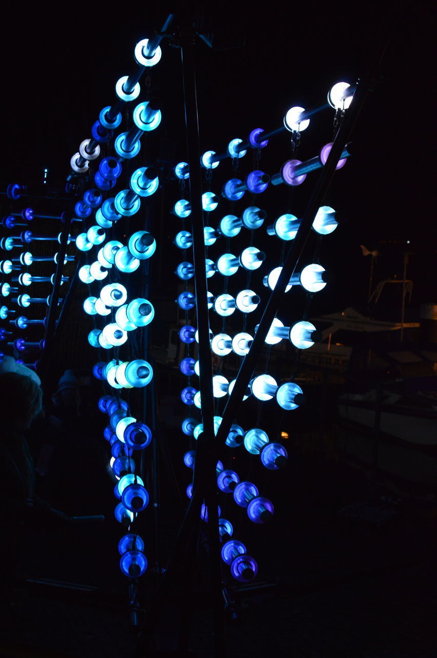 LOW ANGLE VIEW OF ILLUMINATED LIGHTING EQUIPMENT HANGING AT NIGHT