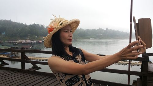 Beautiful mature woman taking selfie with phone on pier over river