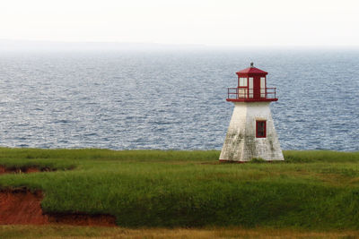 Lighthouse on grassy field by sea