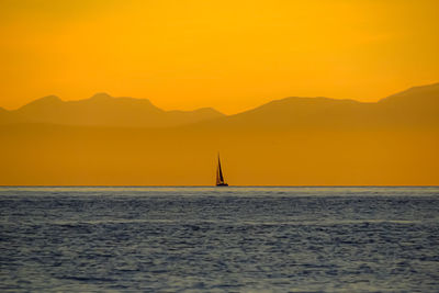 Silhouette sailboat sailing on sea against orange sky