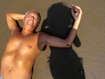 High angle view of shirtless man lying on sand by shadow of woman t beach