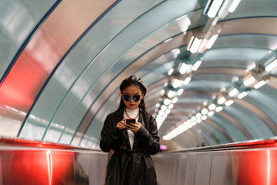 Young lifestyle blogger korean girl posting to social media ride escalator from underground station