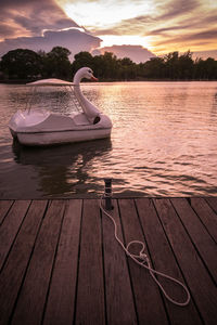 Swan boat in lake against sky during sunset