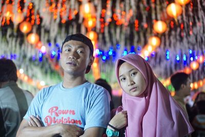 Portrait of friends standing against illuminated lights at night