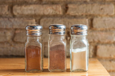 Close-up of various seasoning in bottles on table against brick wall