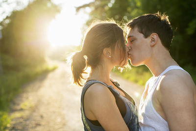 Couple kissing on dirt road against bright sun