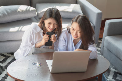 Young woman using smart phone while sitting in laptop