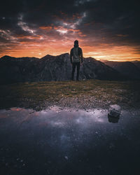 Rear view of man standing on mountain against sky during sunset