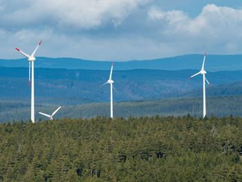 Treetops fo forest and windmill energy farm. summer landscape with green 
wind turbines 