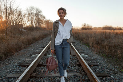 A young woman in a white shirt, beige raincoat and jeans enjoys nature, walking 